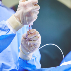 A vet wearing surgical gown and cloves drawing up red fluid through a line and valve port