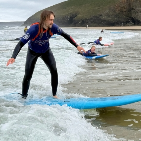 person in a black wetsuit riding a wave on a blue surfboard next to others lying on surfboards